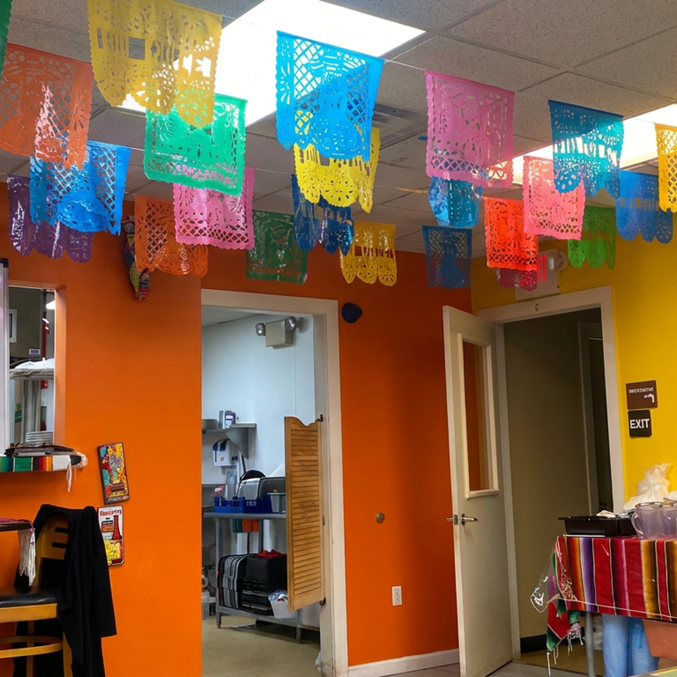 Colorful Mexican papel picado banners decorate a vibrant restaurant dining area with a weekly specials board and coffee station.